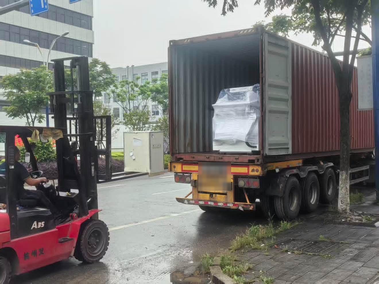 Forklift beside a container with wrapped machinery inside